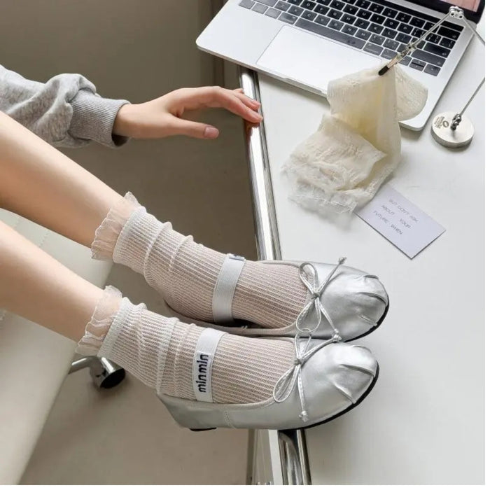 Person wearing white socks with a bow tie design, sitting at a desk with a laptop.