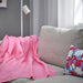 DAGGKÅPOR throw, pink, 130x170 cm. Draped over light grey sofa with floral cushion and white lamp – adds vibrant, cosy touch to warm living room setup – 00598645.