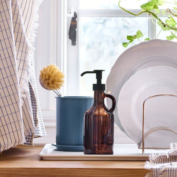 Brown bottle on a windowsill with white plates and a plant in the background