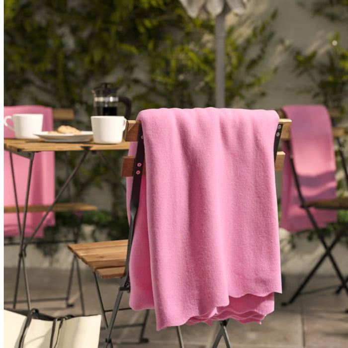 DAGGKÅPOR throw, pink, 130x170 cm. Draped over outdoor chair in garden setting with coffee mugs and French press on table – adds cosy charm to patio mornings – 00598645.