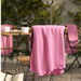 DAGGKÅPOR throw, pink, 130x170 cm. Draped over outdoor chair in garden setting with coffee mugs and French press on table – adds cosy charm to patio mornings – 00598645.