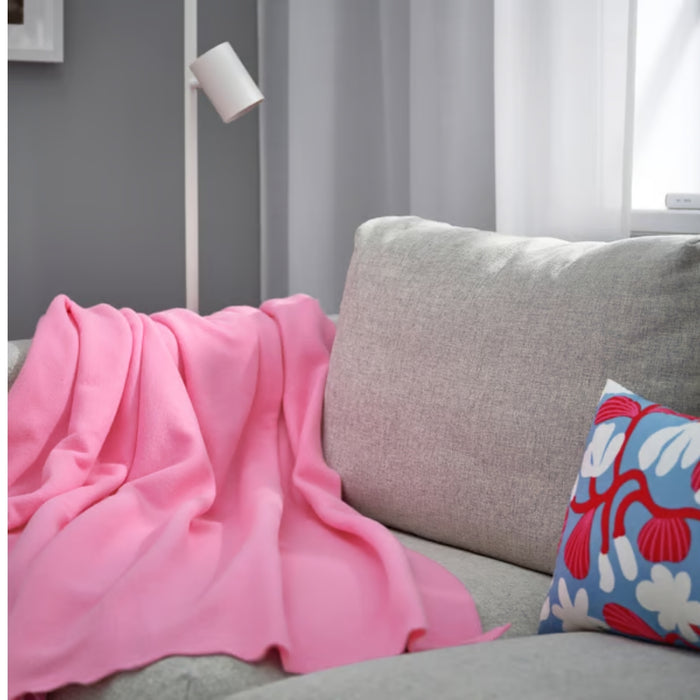 DAGGKÅPOR throw, pink, 130x170 cm. Draped over light grey sofa with abstract cushion, white floor lamp, and grey curtains – adds soft, cosy charm to living room – 00598645.
