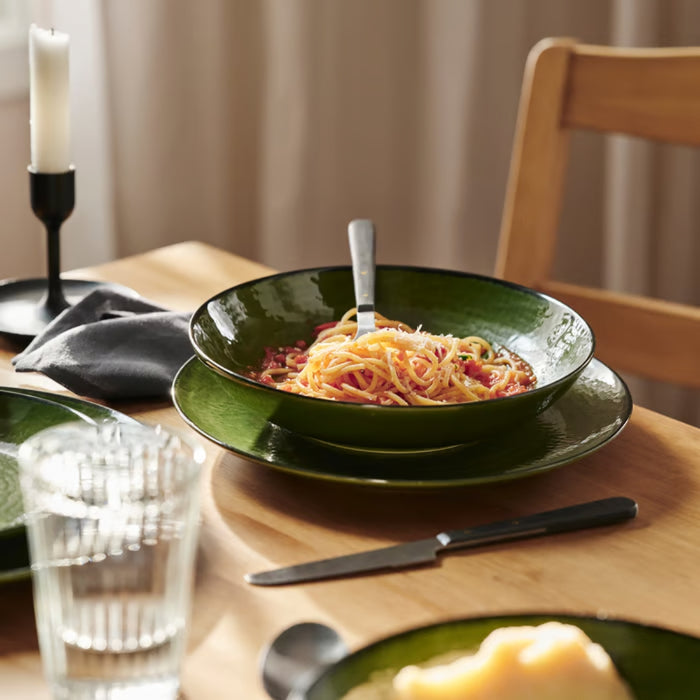 A bowl of pasta with tomato sauce served on a green IKEA PELARKAKTUS plate in a warm, homey dining setting.