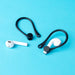 Anti-lost and anti-drop TPU earphone buckle in black—shown on a blue surface with two white wireless earbuds; one earbud is secured inside the black ear hook while the other rests beside it. The buckle’s curved design provides a snug grip to prevent earbuds from falling during movement – 1598446121758 13260401.