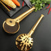 Two golden stainless steel kitchen tongs resting on a sleek black surface. One features a fine mesh strainer with serrated edges, while the other showcases a perforated skimmer head with multiple round and oval holes. Both tools have long, curved handles for safe handling of hot food.- 1600003112384 13034149
