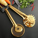 wo golden stainless steel kitchen tongs placed on a black surface—one with a fine wire mesh basket and serrated rim, the other with a starburst-shaped slotted head. Both feature long handles and glossy finishes. Nearby are colorful vegetables including a corn cob, carrot, red chilies, and a bunch of cilantro, evoking a vibrant, food-prep setting ideal for frying, draining, or serving hot dishes. -1600003112384 13034149
