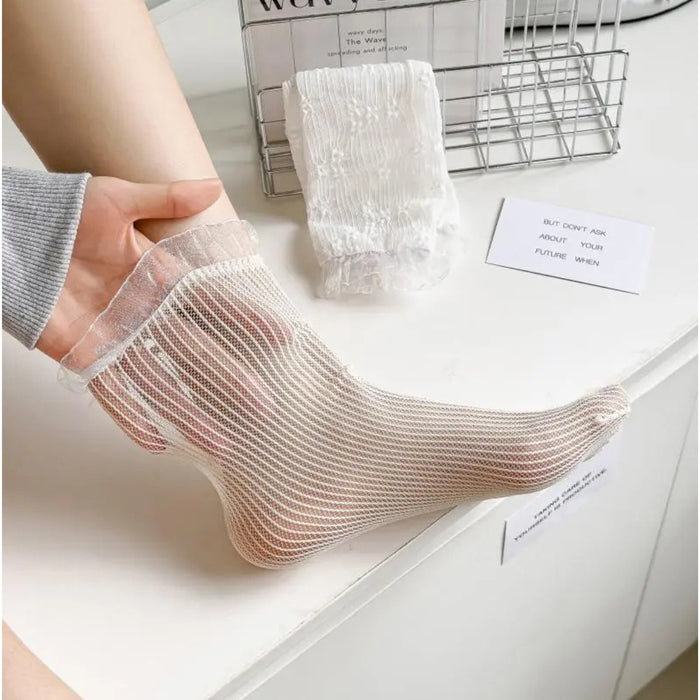 Person wearing sheer white socks on a light surface with a magazine in the background