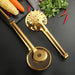 Two golden stainless steel kitchen tools—a mesh strainer tong and a slotted skimmer tong—resting on a dark backdrop. One features a circular wire mesh head with serrated edges, while the other has a starburst perforated design with round holes. Nearby are fresh ingredients: corn cob, carrots, red chilies, and cilantro, arranged on a matte black kitchen tray.- 1600003112384 13034149
