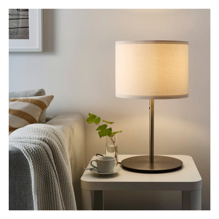 Table lamp on a nightstand next to a bed with a cup and plant