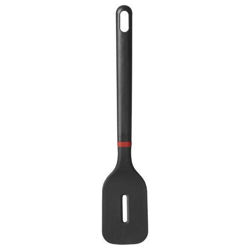 A black kitchen spatula with a rectangular head and a single elongated slot, featuring a dark gray handle with a red accent near the joint, resting on a light gray surface