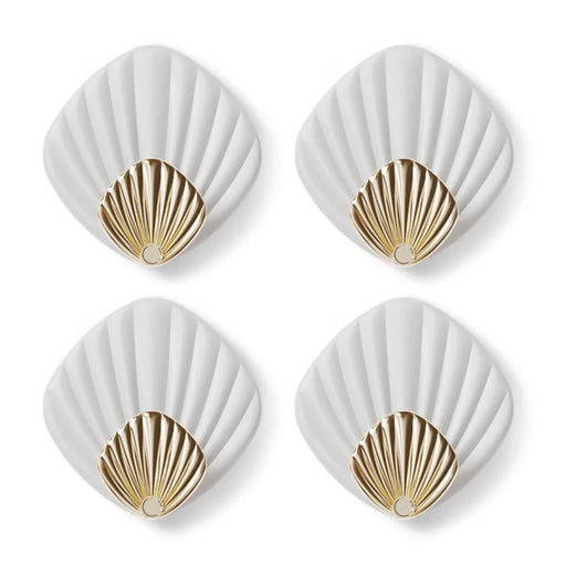 Four white coasters with gold shell designs on a white background