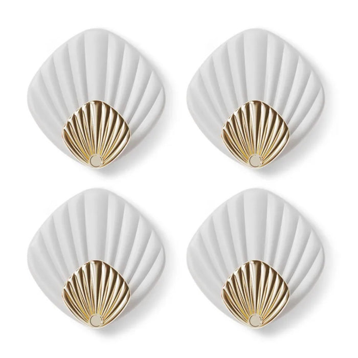 Four white coasters with gold shell designs on a white background