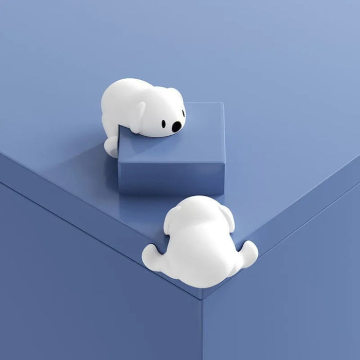 Two white silicone corner guards shaped like adorable cartoon puppies are attached to the corner of a blue surface—one on the top and one on the side. Their soft, rounded design adds charm while providing child-safe edge protection. Ideal for homes with toddlers, these guards serve both as safety tools and playful décor accents -1600001888980 13025258.