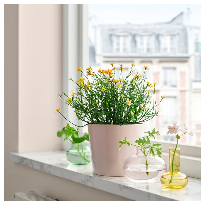 Small yellow IKEA FEJKA artificial plant in a pink pot used as a decorative accent on a marble windowsill.
