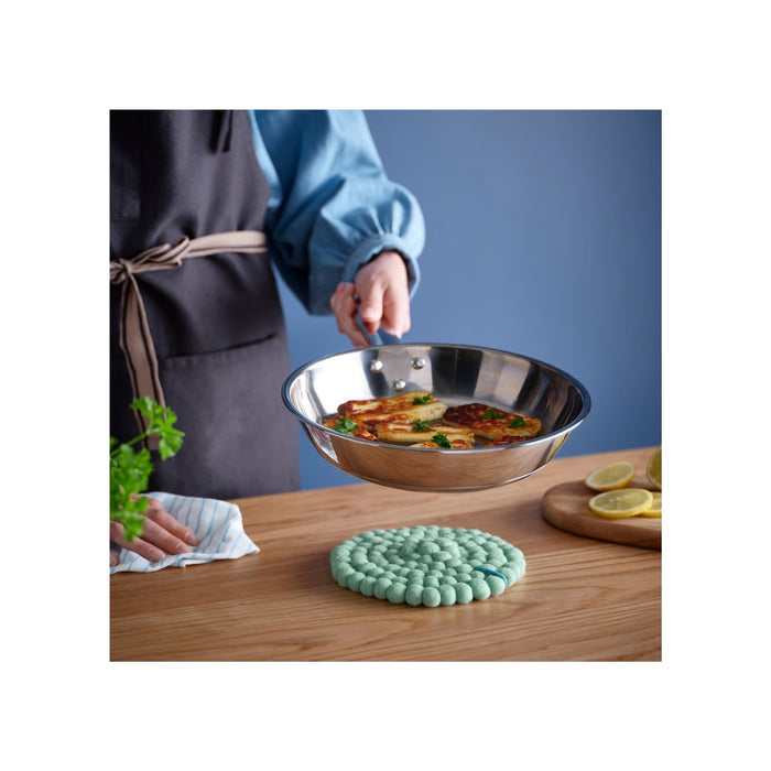 Person holding a metal bowl with food on a wooden table, wearing an apron.