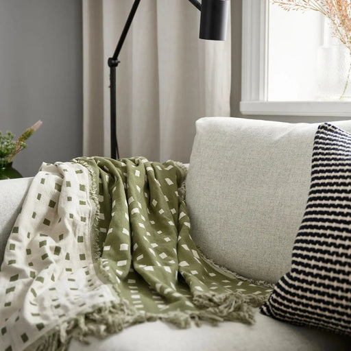 SVARTTÅG throw draped over armrest of light grey sofa, paired with striped cushion and soft lighting for cozy decor