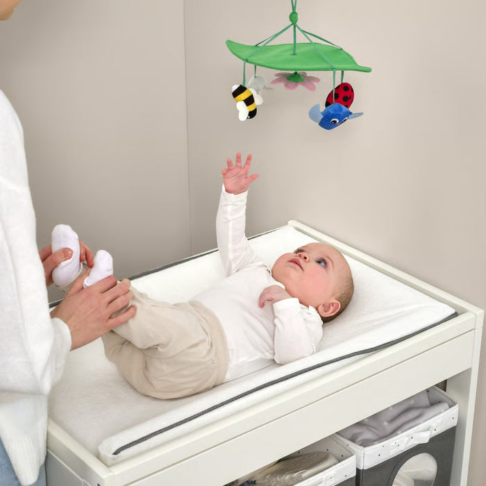 Baby lying on changing table reaching for SANDBI mobile with bee, ladybug, fish, and flower plush toys