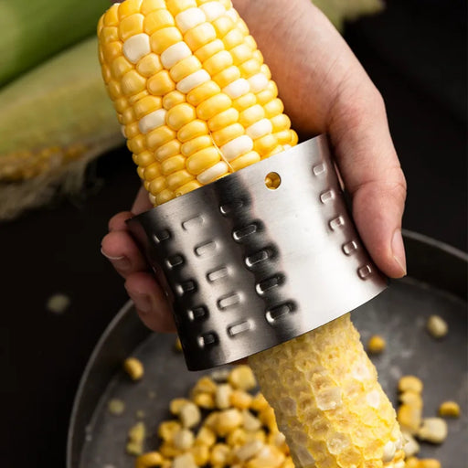 Corn on the cob being grated with a metal tool over a dark surface.