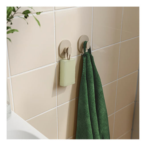 Two hooks on a tiled wall with a green towel and small container.