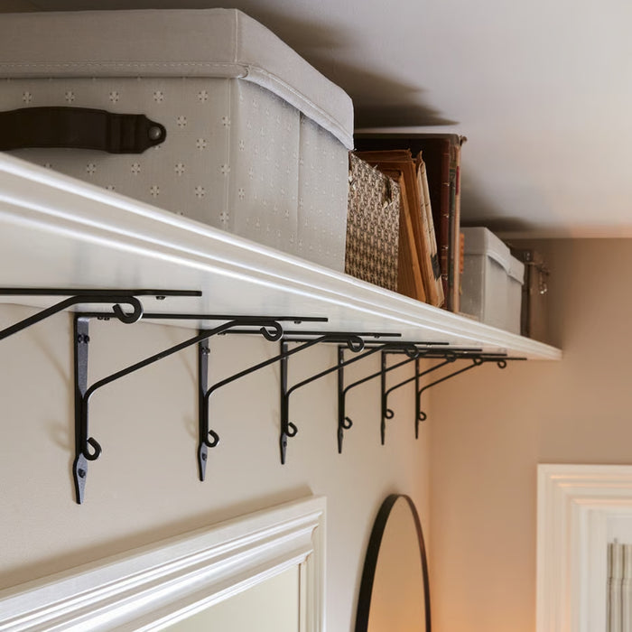Shelf with decorative brackets and storage boxes against a neutral wall.