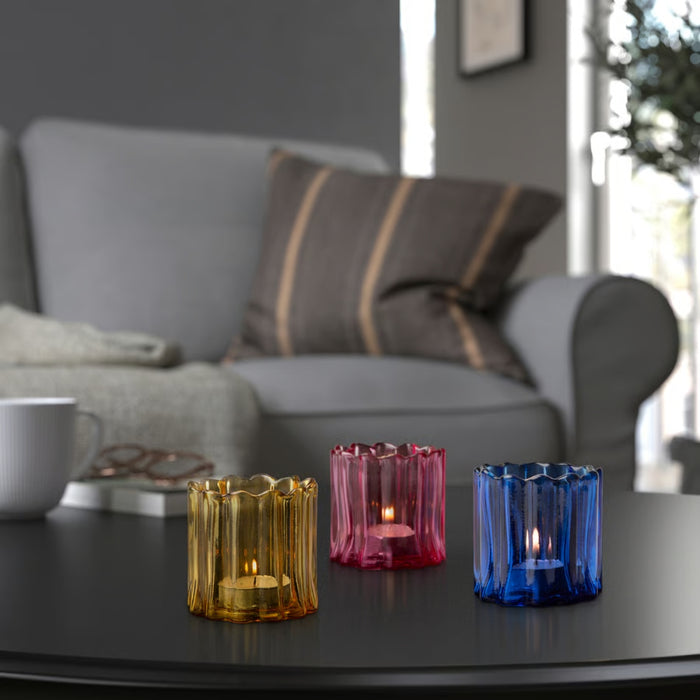 Three colorful glass candle holders on a table with a blurred living room background