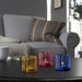 Three colorful glass candle holders on a table with a blurred living room background