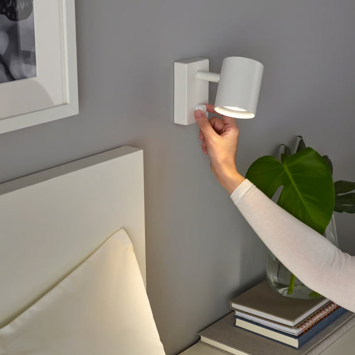 Hand adjusting a wall-mounted light fixture on a gray wall.