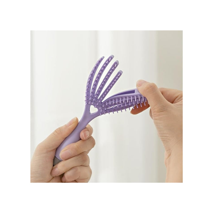 Purple hairbrush with heart design held by a hand against a white background