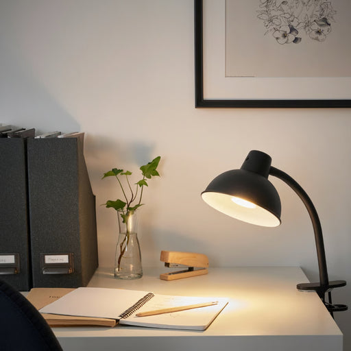 Desk setup with lamp, notebook, pen, and plant in a home office setting.
