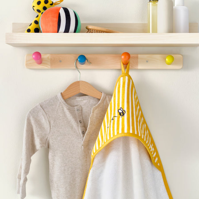 Children's clothing and a yellow bib hanging on a wooden peg rail with colorful hooks.