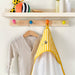 Children's clothing and a yellow bib hanging on a wooden peg rail with colorful hooks.