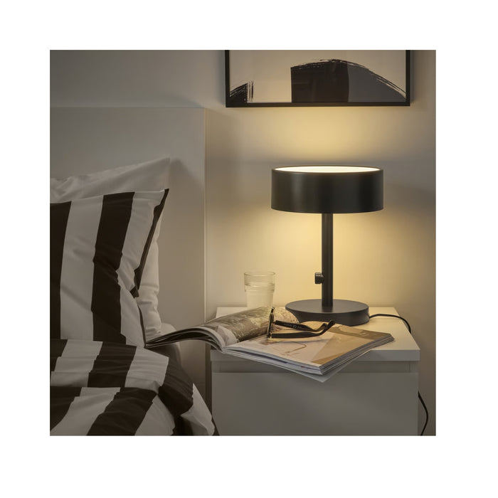 Black table lamp on a nightstand next to a bed with striped bedding.