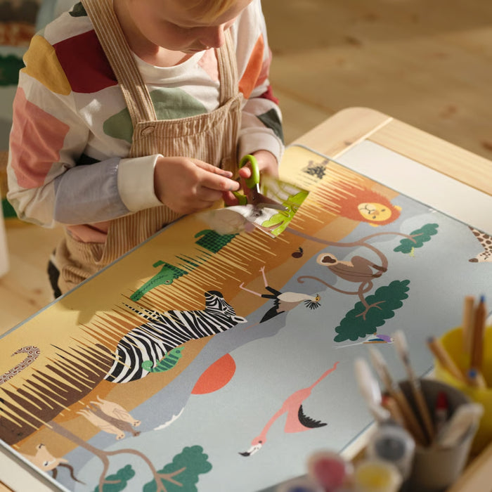 Child painting on a large sheet of paper with animal designs, surrounded by art supplies.
