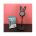 Black bunny ear phone stand with packaging on a pink background