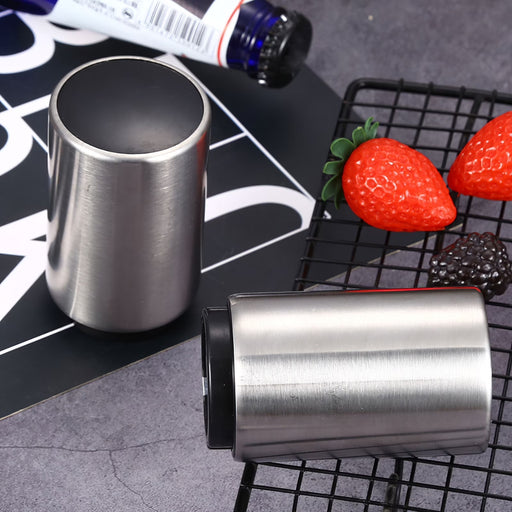 Two Bottle Openers on a black surface with strawberries and a bottle in the background.
