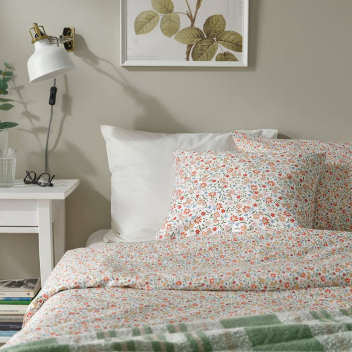 GULLNATTLJUS cushion cover, white/floral, 50x50 cm. Shown on bed with matching bedding and green checkered throw. Adds cosy, colourful touch to bedroom – 90598702.