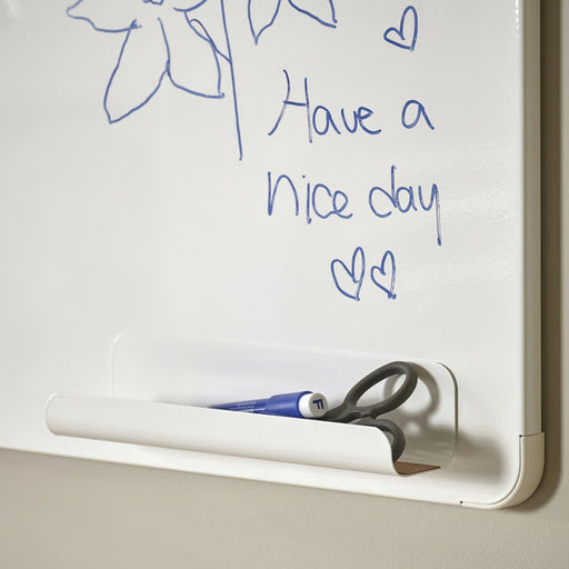  A whiteboard with a handwritten message in blue marker reading “Have a nice day,” decorated with two small hearts and a simple flower sketch. A tray below holds scissors and a blue marker