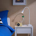 Nighstand with lamp, clock, and glass on a wooden nightstand next to a bed with blue bedding.
