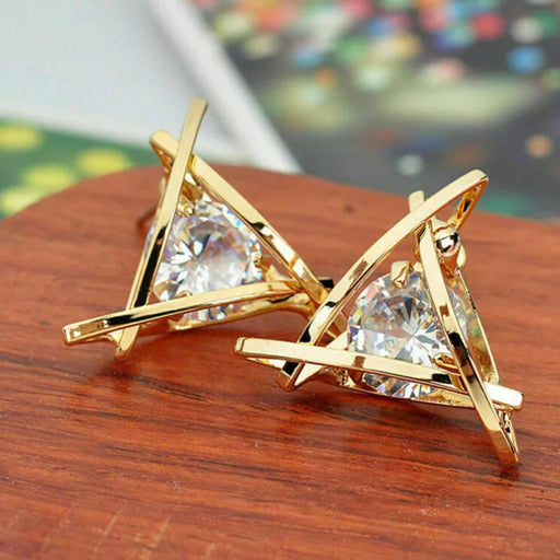 Triangle gold earrings – abstract gold cage earrings with triangular-cut crystal, displayed on wooden surface with festive lights

