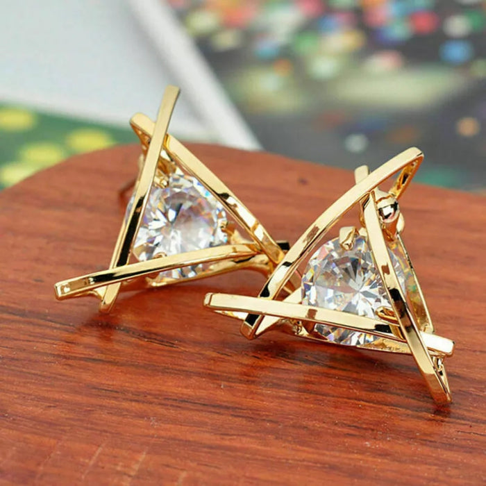 Triangle gold earrings – abstract gold cage earrings with triangular-cut crystal, displayed on wooden surface with festive lights


