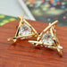 Triangle gold earrings – abstract gold cage earrings with triangular-cut crystal, displayed on wooden surface with festive lights

