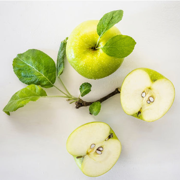 A fresh green apple, whole and sliced in half, revealing its seeds, placed alongside a small branch with green leaves. The natural composition highlights the vibrant color and freshness of the apple, making it a visually appealing representation of crisp fruit-90582065