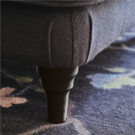 Close-up of ESSEBODA leg installed on upholstered furniture, blending with textured fabric and patterned rug for elegant finish