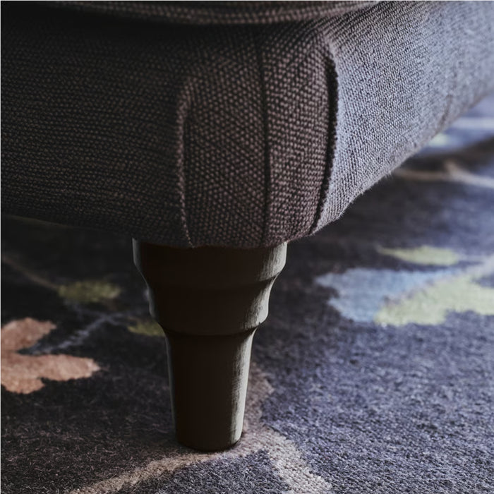 Close-up of ESSEBODA leg installed on upholstered furniture, blending with textured fabric and patterned rug for elegant finish