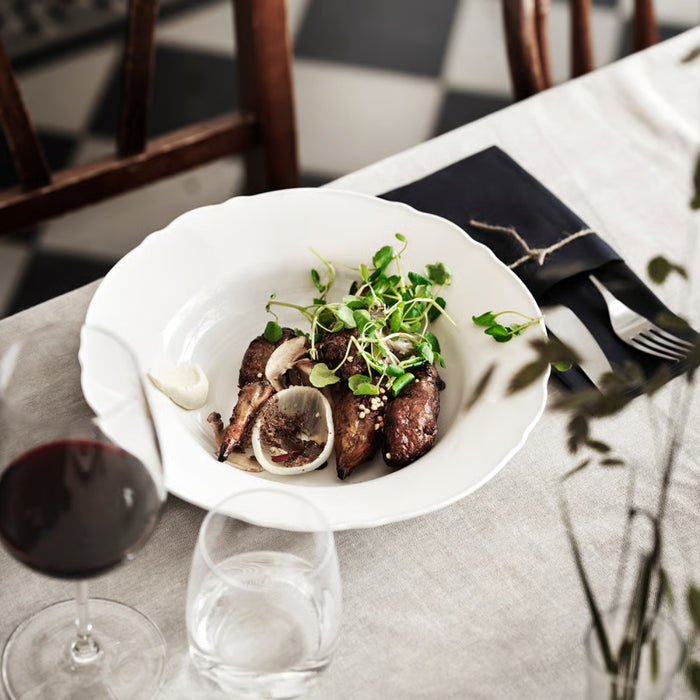 ining table setting featuring an IKEA UPPLAGA deep plate with a gourmet meal, alongside a glass of red wine, a water glass, and black table linens—ideal for elegant dining and food presentation.-30424719