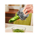 Person using a vegetable peeler to slice a cucumber over a glass bowl on a kitchen counter.