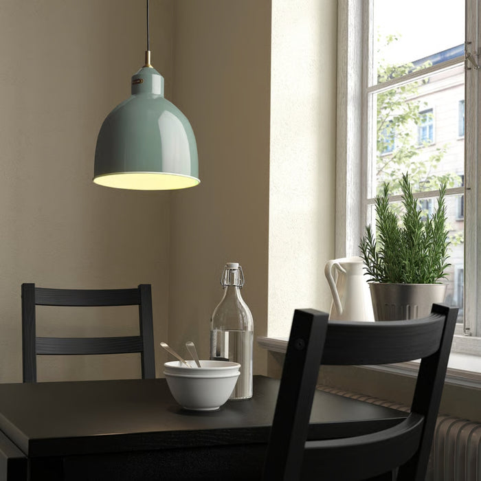 RÖDFLIK pendant lamp styled above dining nook with black table and chairs, glowing warm light over bowl and glass bottle