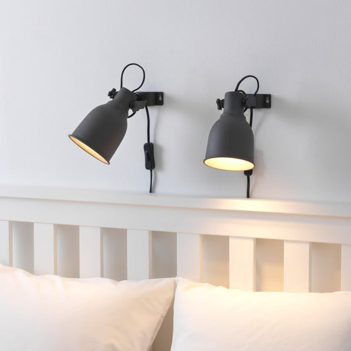 Two black wall-mounted lamps on a white wall above a bed.