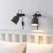 Two black wall-mounted lamps on a white wall above a bed.