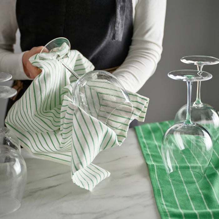 Person cleaning a glass with a green and white striped cloth on a marble surface.